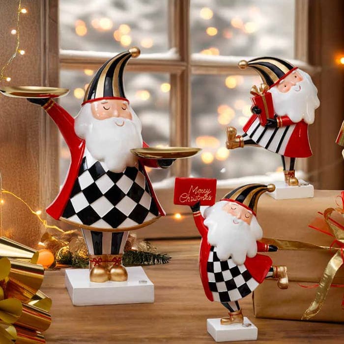 Tre figure di Babbo Natale Fantin Argenti in finitura rossa, bianca e nera disposte su una mensola con luci natalizie sullo sfondo.